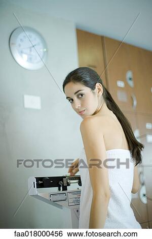 Stock Photograph - Woman wrapped in towel, standing on scale, looking at camera. Fotosearch