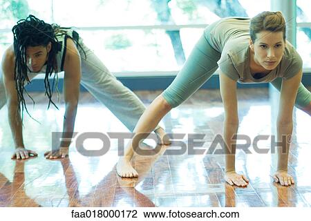 Stock Image - Young adults doing prasarita padottanasana pose in yoga class. Fotosearch
