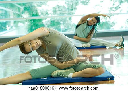Stock Photo - Young adults doing side stretch in exercise class. Fotosearch