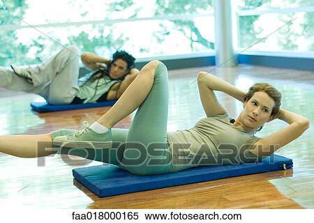 Stock Photography - Young adults doing sit-ups in exercise class. Fotosearch