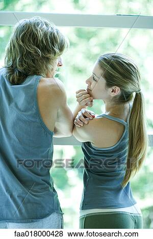 Stock Photo - Young couple in exercise clothes, standing by window, rear view. Fotosearch