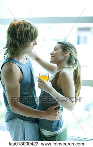 Stock Image - Young couple in exercise clothing standing by window, embracing. Fotosearch