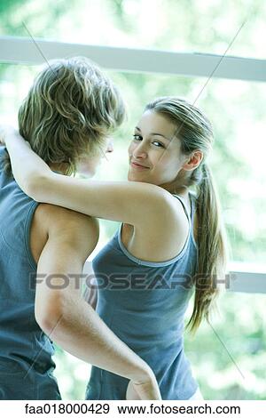 Stock Photo - Young couple in exercise clothing standing by window, woman looking over shoulder, smiling at camera. Fotosearch