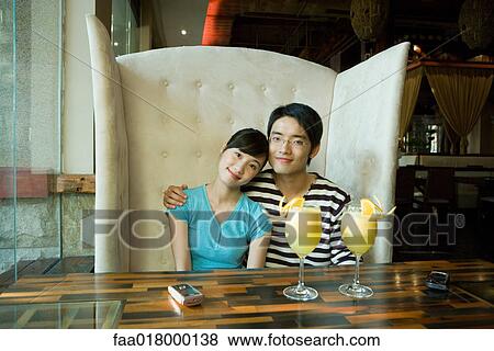 Stock Photo - Young couple sitting in booth, cocktails on table, smiling at camera. Fotosearch