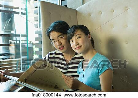 Young couple sitting in restaurant, holding menu View Large Photo Image Picture - Young couple sitting in restaurant, holding menu. Fotosearch