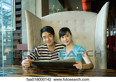 Stock Image - Young couple sitting in restaurant, holding menu. Fotosearch