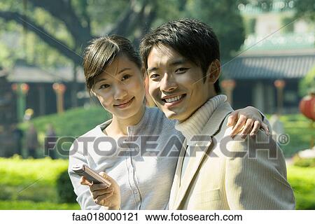 Young couple with cell phone, smiling at camera, portrait View Large Photo Image Stock Image - Young couple with cell phone, smiling at camera, portrait. Fotosearch