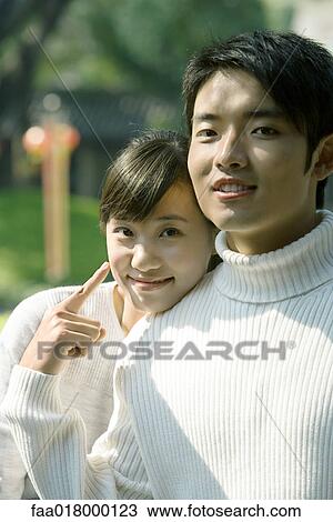 Young couple, woman resting head on man's shoulder, man pointing to woman, both smiling at camera View Large Photo Image Stock Image - Young couple, woman resting head on man's shoulder, man pointing to woman, both smiling at camera. Fotosearch