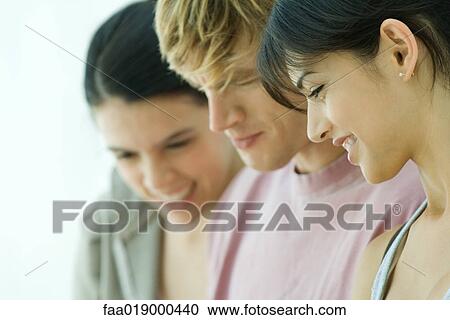 Stock Image - Young friends, looking down, close-up . Fotosearch