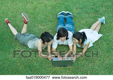 Stock Photo - Young friends lying in grass, using laptop together. Fotosearch