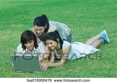 Stock Photo - Young friends lying in grass, using laptop together. Fotosearch