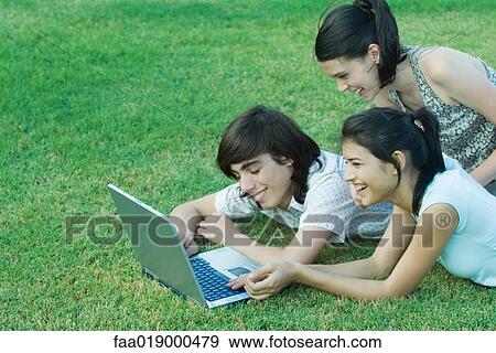 Young friends lying in grass, using laptop together View Large Photo Image Stock Photo - Young friends lying in grass, using laptop together. Fotosearch