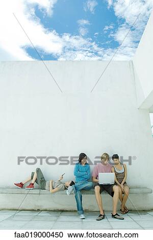 Young friends sitting outdoors, using laptop View Large Photo Image Stock Image - Young friends sitting outdoors, using laptop. Fotosearch