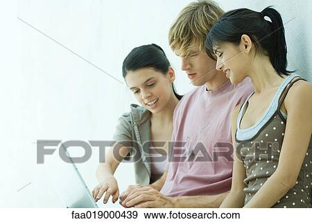 Stock Photo - Young friends using laptop together. Fotosearch