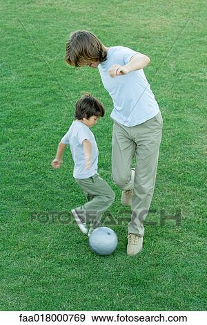 Stock Photo - Young man and boy playing soccer on lawn, high angle view. Fotosearch