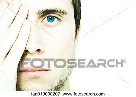 Stock Photo - Young man covering one eye, looking at camera, extreme close-up. Fotosearch