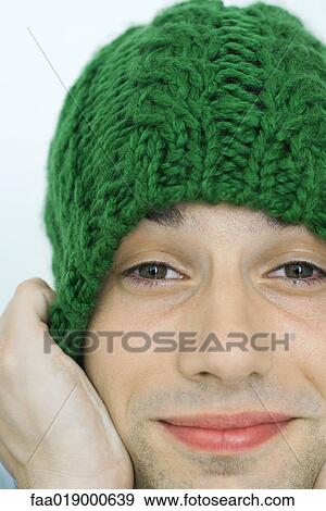 Stock Photo - Young man pulling down knit hat over ears, portrait, close-up. Fotosearch