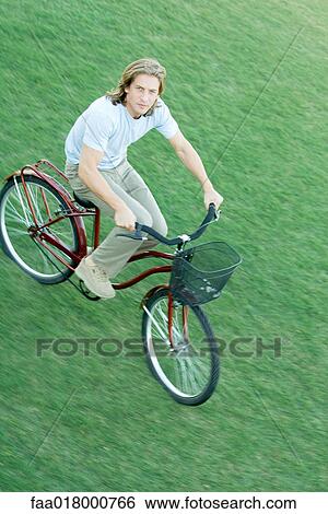 Stock Photograph - Young man riding bicycle across grass. Fotosearch