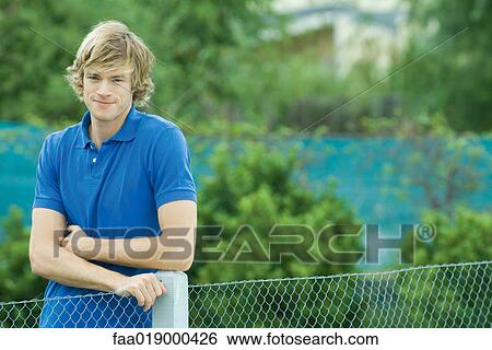 Young man standing next to fence, smiling at camera View Large Photo Image Stock Photograph - Young man standing next to fence, smiling at camera. Fotosearch