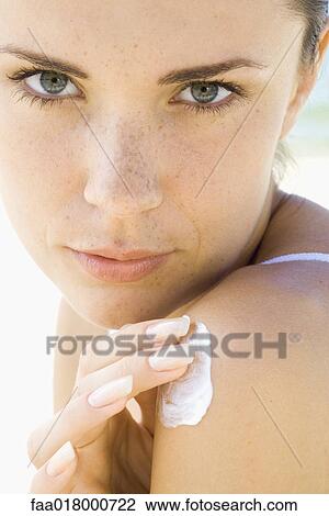 Stock Image - Young woman applying sunscreen to shoulder. Fotosearch
