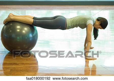 Young woman doing push-ups with legs resting on fitness ball View Large Photo Image Stock Image - Young woman doing push-ups with legs resting on fitness ball. Fotosearch