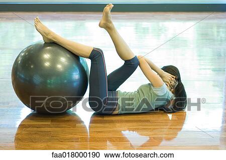 Young woman doing sit-ups with legs resting on fitness ball View Large Photo Image Stock Image - Young woman doing sit-ups with legs resting on fitness ball. Fotosearch