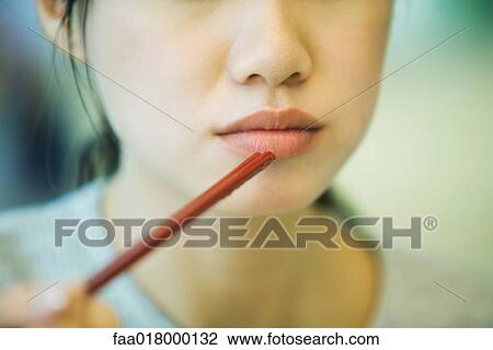 Stock Image - Young woman eating with chopsticks. Fotosearch
