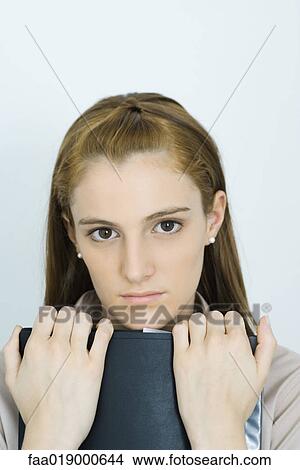 Young woman, holding binder against chest, looking at camera, portrait View Large Photo Image Picture - Young woman, holding binder against chest, looking at camera, portrait. Fotosearch