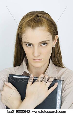 Young woman, holding binder against chest, looking at camera, portrait View Large Photo Image Stock Image - Young woman, holding binder against chest, looking at camera, portrait. Fotosearch