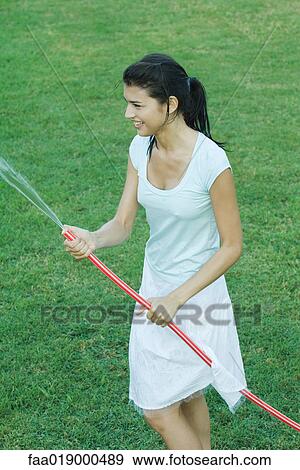 Stock Photo - Young woman holding garden hose. Fotosearch