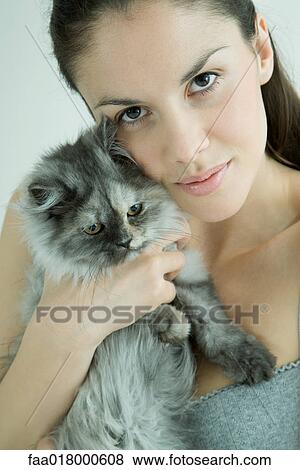 Young woman holding up cat to cheek, smiling at camera View Large Photo Image Stock Photo - Young woman holding up cat to cheek, smiling at camera. Fotosearch
