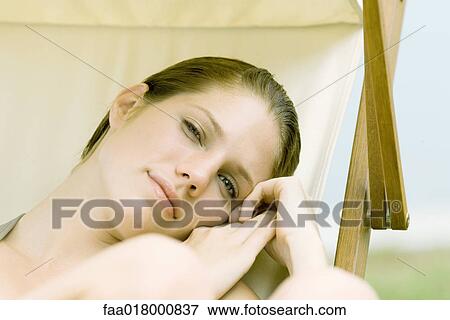 Stock Photo - Young woman lounging in beach chair, looking at camera. Fotosearch