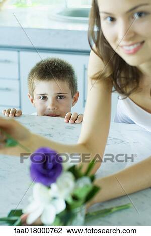 Stock Image - Young woman making fresh flower arrangement, next to boy, smiling. Fotosearch