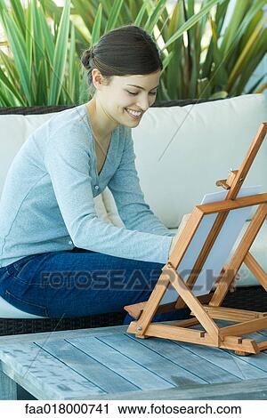 Stock Image - Young woman painting with easel. Fotosearch
