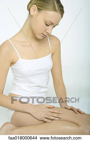 Young woman sitting in tank top and underwear, touching legs View Large Photo Image Picture - Young woman sitting in tank top and underwear, touching legs. Fotosearch