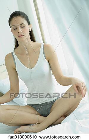 Young woman sitting indian style on bed, eyes closed, listening to earphones View Large Photo Image Stock Image - Young woman sitting indian style on bed, eyes closed, listening to earphones. Fotosearch