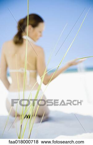 Young woman sitting on beach, focus on dune grass in foreground View Large Photo Image Stock Photo - Young woman sitting on beach, focus on dune grass in foreground. Fotosearch