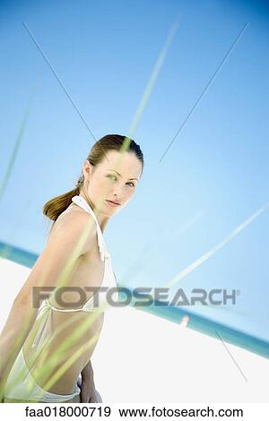 Stock Photo - Young woman sitting on beach, focus on dune grass in foreground. Fotosearch