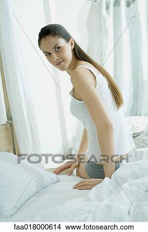 Young woman sitting on edge of bed, looking over shoulder View Large Photo Image Picture - Young woman sitting on edge of bed, looking over shoulder. Fotosearch