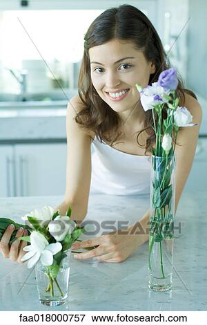 Stock Photo - Young woman smiling, with fresh flowers in vases, portrait. Fotosearch