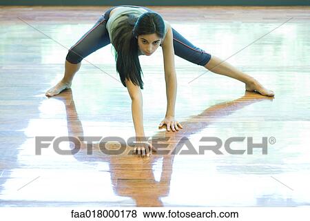 Stock Photo - Young woman standing with legs apart, palms flat on floor. Fotosearch