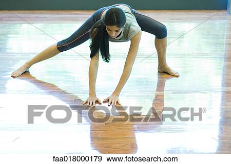 Stock Photo - Young woman standing with legs apart, palms flat on floor. Fotosearch