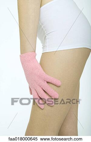 Stock Photography - Young woman touching leg with massage glove, close-up of mid-section. Fotosearch