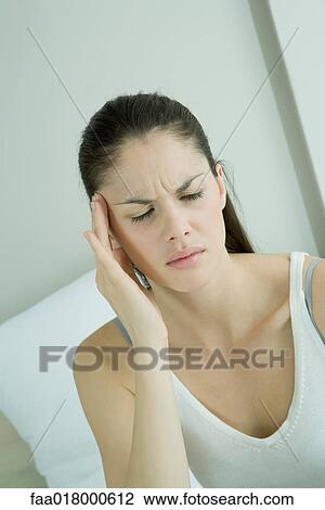 Stock Image - Young woman touching temple, furrowing brow. Fotosearch