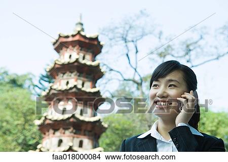 Young woman using cell phone, pagoda in background View Large Photo Image Picture - Young woman using cell phone, pagoda in background. Fotosearch