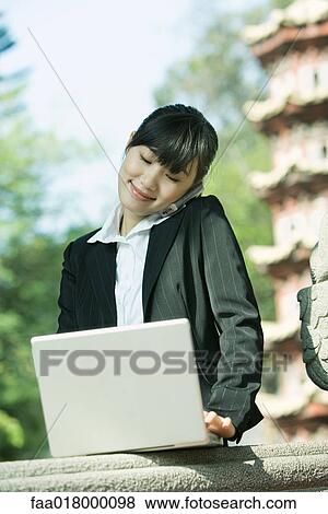 Young woman using laptop and cell phone View Large Photo Image Stock Photo - Young woman using laptop and cell phone. Fotosearch