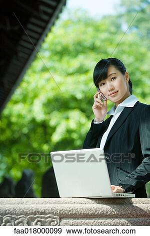 Young woman using laptop and cell phone View Large Photo Image Stock Photo - Young woman using laptop and cell phone. Fotosearch