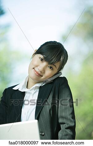 Young woman using laptop and cell phone, smiling at camera View Large Photo Image Stock Photo - Young woman using laptop and cell phone, smiling at camera. Fotosearch