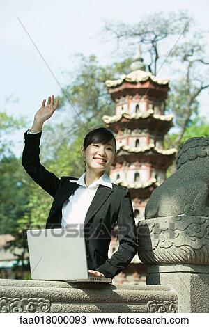 Stock Image - Young woman using laptop, waving. Fotosearch