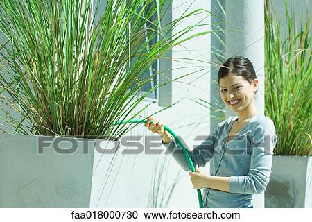 Stock Image - Young woman watering plants with garden hose. Fotosearch